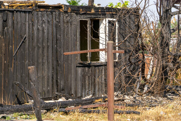 Burnt wooden building with charred walls and empty window frames, destroyed by fire, surrounded by...