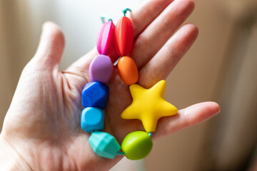 Colorful silicone teether bracelet held in hand. This chewable toy features bright and vibrant shapes, designed to stimulate sensory development and soothe teething infants.
