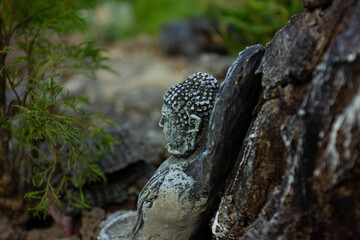 Close-up of an old, weathered stone Buddha statue in a tranquil garden. An image of meditation,...
