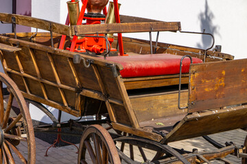 Vintage wooden fire cart with a manual pump and red seat, mounted on wooden spoked wheels,...