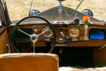 Interior of a vintage car with a wooden dashboard, classic steering wheel, and a single rose in a...