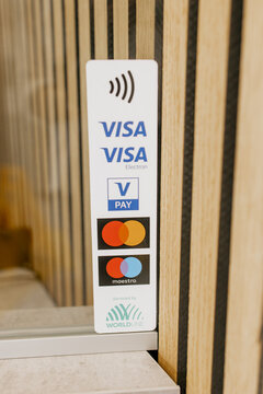 Close-up of a payment acceptance sign displaying contactless logos and supported cards including Visa, Visa Electron, V Pay, Mastercard, and Maestro, on a wooden wall background at a retail or service