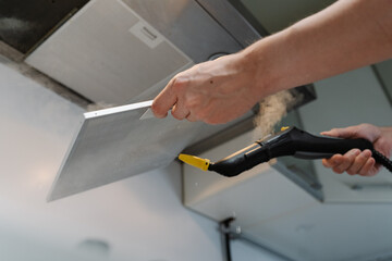 Close-up low-angle view of homeowner disinfecting kitchen extractor filter using steam cleaner in modern kitchen, ensuring hygiene and cleanliness. Concept of easy housekeeping domestic life, closeup.