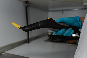 Professional cleaning specialist wearing blue protective gloves holding steam cleaner, preparing to...