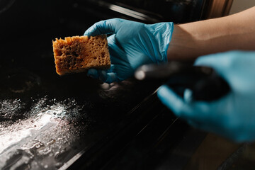 Professional kitchen worker wearing blue gloves spraying detergent on sponge, preparing to clean...