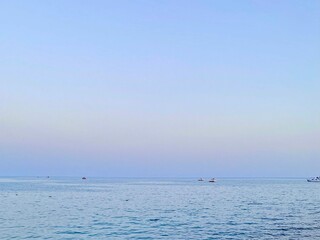Tranquil sea view at sunset in Antalya, Turkey. Minimalist composition with calm water, small boats, and soft pastel sky. Peaceful Mediterranean evening scenery.