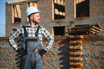 Male construction worker in uniform and helmet on construction of red brick house