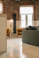 Bright loft-style living space with mustard armchairs, white table, gray sofa, exposed red brick...
