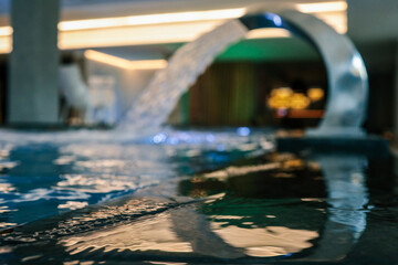 Close-up view of relaxing indoor pool with flowing water from a curved fountain. Gentle reflections...