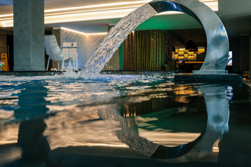 Close-up view of relaxing indoor pool with flowing water from a curved fountain. Gentle reflections...