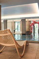 Modern indoor pool area with a stylish white lounge chair in the foreground, reflecting calm water and ambient ceiling lights. Elegant spa interior with floral arch and natural daylight