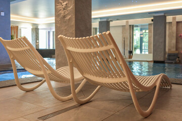 Two modern white lounge chairs by the edge of an indoor pool in a stylish spa area. Soft lighting, serene atmosphere, and elegant architectural details create a relaxing environment