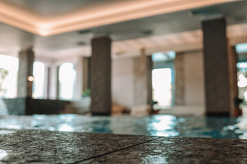 Close-up of a textured stone pool edge with a blurred view of a luxurious indoor spa and pool area...
