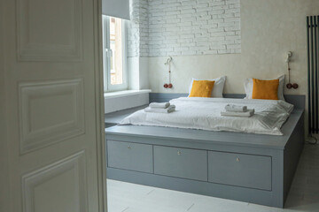 Modern minimalist bedroom with a gray platform bed, yellow accent pillows, white brick and plaster wall, large windows, and soft natural light. Neat, cozy and stylish design