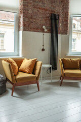 Stylish loft interior with two mustard yellow armchairs, pillows, a white side table, brick and...