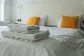 Folded white towels on a neatly made bed with white linens and yellow pillows in a bright modern...