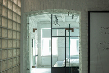 Bright modern bedroom interior with white painted brick walls, large windows, and a glass partition...
