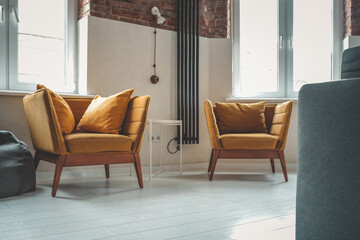 Stylish modern interior with two mustard yellow armchairs, accent pillows, white floor, brick and...