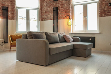 Modern living room with gray L-shaped sofa, mustard yellow armchair, exposed brick walls, tall...