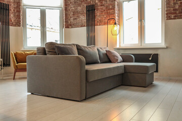 Modern living room with gray L-shaped sofa, mustard yellow armchair, exposed brick walls, tall...