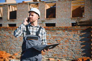 Engineer, bearded man wears safety helmet inspecting housing development project at construction...