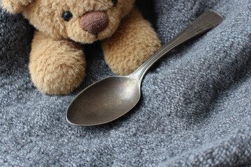 Teddy bear steel spoon burnished edge soft fabric cozy plush grey blanket childhood comfort relaxation closeup warmth innocence gentle home texture metal toy nap peaceful domestic cute fuzzy