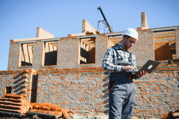Engineer, bearded man wears safety helmet inspecting housing development project at construction...