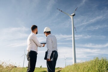 Looking far away, planning. Two men engineers are on field, with wind turbines