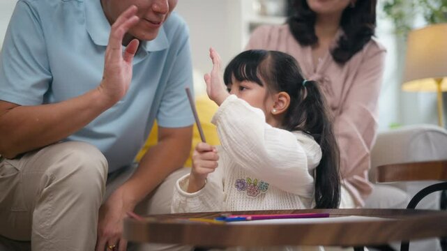 Father encouraging his daughter&rsquo;s artwork with a high-five at home.father praising young daughter for her drawing sitting together at home.Concept of positive parenting,family bonding,child creativity