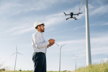 Modern drone is flying. Male engineer in field checking on wind turbine production