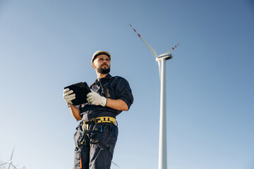 Against blue sky. Engineer in field checking on wind turbine production