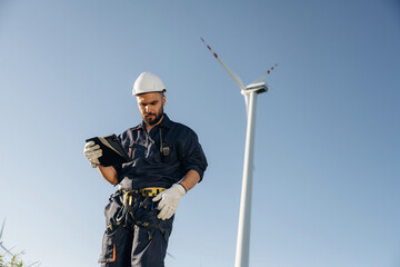 Against blue sky. Engineer in field checking on wind turbine production