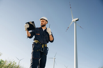 Giving orders by using walkie talkie. Engineer in field checking on wind turbine production