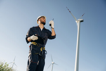 Giving orders by using walkie talkie. Engineer in field checking on wind turbine production