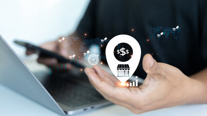Hand holding mobile phone and location icon with store and dollar sign, symbolizing e-commerce...