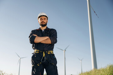 Standing with arms crossed. Engineer in field checking on wind turbine production