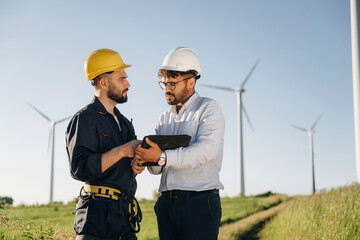 Cooperation concept. Two men engineers are on field, with wind turbines