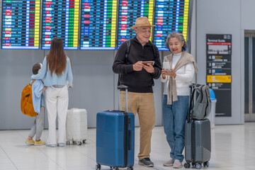 asian senior couple passengers with suitcase and backpack standing at departure schedule,check gate and boarding time on smartphone for going to the plane,elderly with modern lifestyle,travel