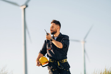Technician is giving orders by walkie talkie. Engineer in field checking on wind turbine production