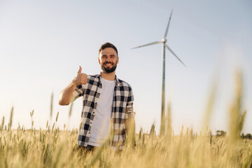 In checkered shirt. Guy engineer in wheat field against wind turbines