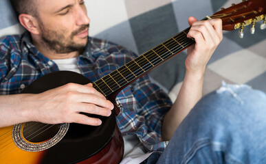 A young man plays the guitar while relaxing at home. Concept of music hobby, relaxation, creativity and home practice. Selective focus.
