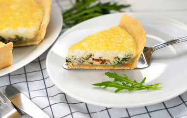 Close-up of a slice of homemade Quiche Lorraine with spinach, cheese and vegetables served on a white plate. Selective focus.