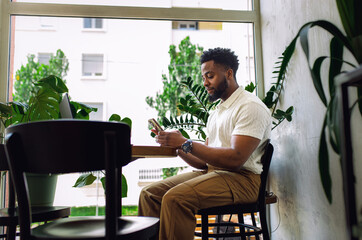 Smiling man sitting in coffee shop looking at his samrtphone.