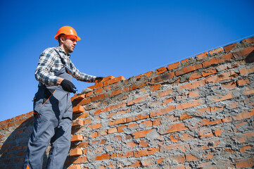 Bricklayer industrial worker installing brick masonry on exterior wall with trowel putty knife