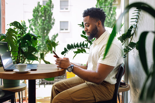 Smiling man sitting in coffee shop looking at his samrtphone.