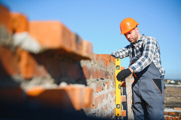 construction mason worker bricklayer installing red brick with trowel putty knife outdoors