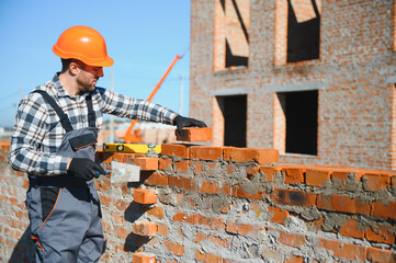 Bricklayer industrial worker installing brick masonry on exterior wall with trowel putty knife