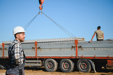 A builder controls a crane while unloading panels to cover a house