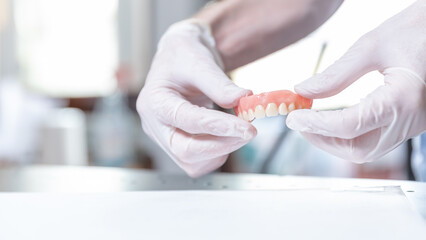 Upper denture held between both gloved hands in dental clinic  
