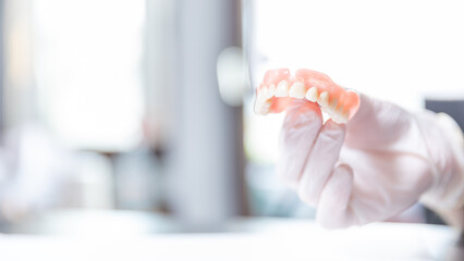 Dentist holding upper denture between fingers in bright clinic    © SWMedia